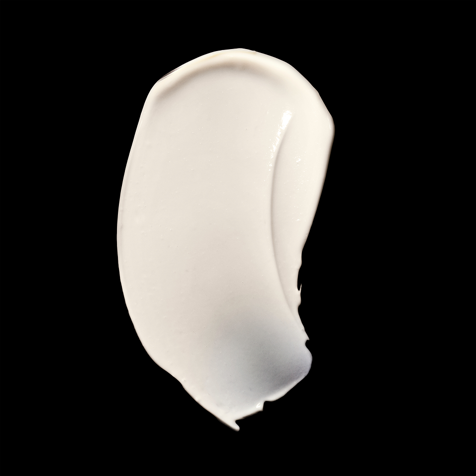 A thick, creamy white swatch of cosmetic cream or lotion on a solid black background.